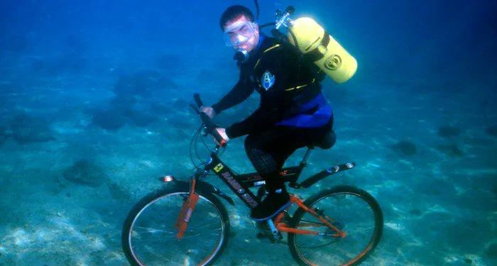 Scuba diver underwater riding a bicycle, humorous visual for personal watercraft article